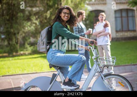 A smiling young mulatta riding a bike and feeling cheerful Stock Photo
