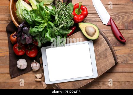 Digital recipe book, greens, vegetables and knife on wooden background Stock Photo