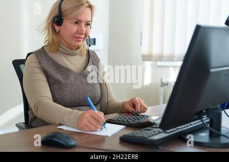 Financial data analyzing. Close-up photo of a businesswoman writing and counting on calculator in office. Selective focus. Stock Photo