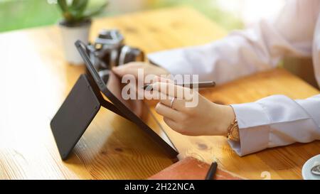 Close-up female hands using stylus pen drawing on portable digital tablet screen on working desk. Stock Photo