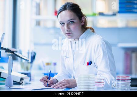 Lab technician with sample in petri dish works in a lab with lab equipment and writes protocol, Freiburg, Baden-Wuerttemberg, Germany Stock Photo