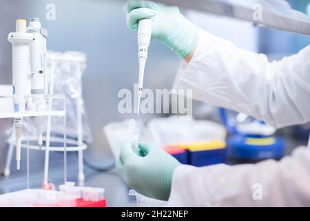 Young lab technician wearing a face mask and pipetting a sample in a laboratory with laboratory equipment at a workflow, Freiburg Stock Photo