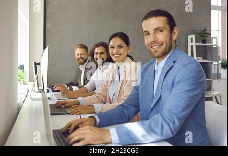 Portrait of confident team working together sitting in row next to each other in office. Stock Photo
