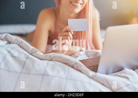Smiling woman with holds blank credit card near laptop during online shopping o bed Stock Photo