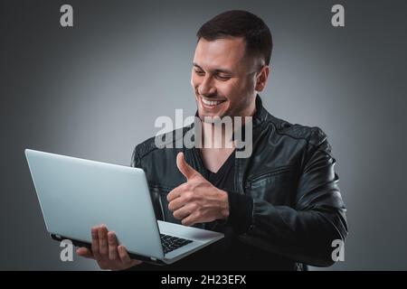 Portrait of young handsome man using laptop, wearing black leather jacket. Stock Photo