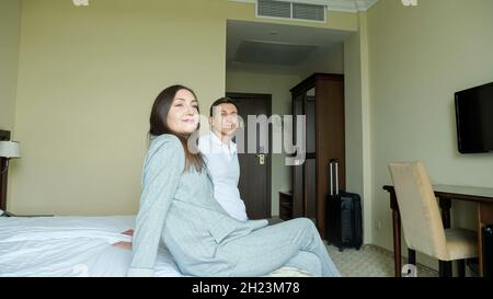 young couple with a suitcase enter the hotel room and sit on the bed Stock Photo