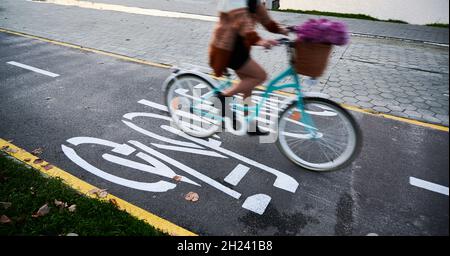 Motion blur woman stylish dressed riding blue bicycle on bike lane with pink bouquet flowers. Concept of walk on bicycle in centre city or park in autumn in good weather. Stock Photo