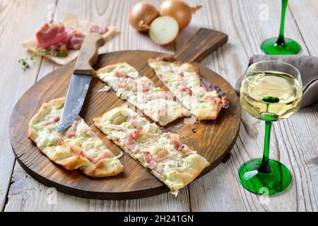 Typical tarte flambée from Alsace with sour cream, onions and smoked bacon hot from the oven, served with Alsatian white wine Stock Photo