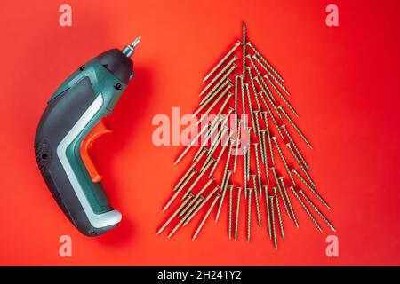 Long golden self-tapping screws, laid out in shape of Christmas tree and screwdriver on red background Stock Photo