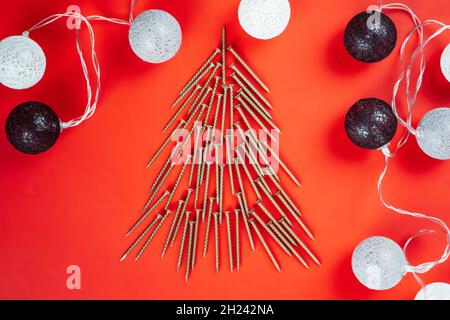 Long golden self-tapping screws, laid out in shape of Christmas tree and ball garland on red background Stock Photo