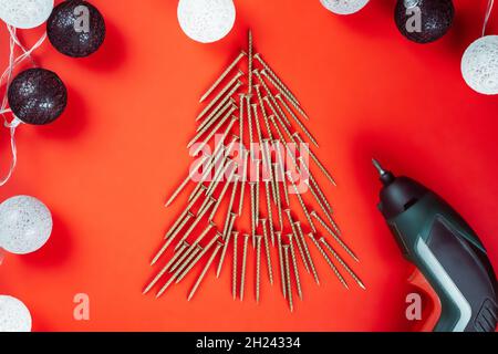 Long golden self-tapping screws, laid out in shape of Christmas tree, screwdriver and ball garland on red background Stock Photo