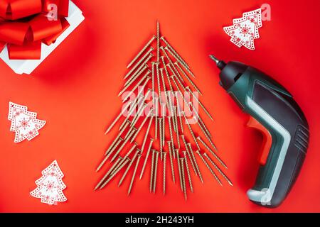 Long golden self-tapping screws, laid out in shape of Christmas tree, screwdriver and gift box on red background Stock Photo