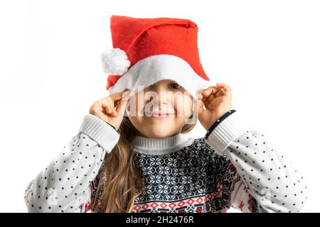 portrait of girl in white knitted Christmas sweater with reindeer hiding half face in Santa Claus hat, isolated on white background Stock Photo