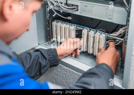 A man electrician checks the terminals of telephone communication equipment. The specialist serves the node of the telephone line. Authentic work-like scene. Stock Photo