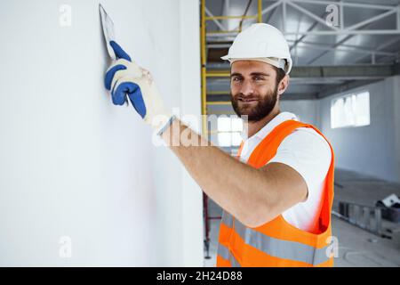 Plasterer in workwear smoothing wall surface of building indoors Stock Photo