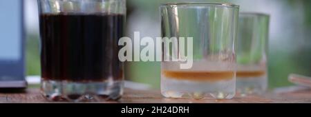 Two transparent glass glasses full of dark liquid and empty stand on table Stock Photo