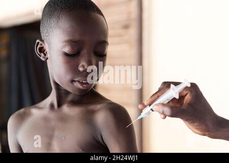 Black nurse explaining injection tool to a young attentive looking African schoolboy during antimalarial vaccination Stock Photo