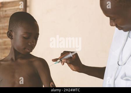 In this image, a doctor is explaing to a small confident looking black boy what happens during malaria vaccination Stock Photo