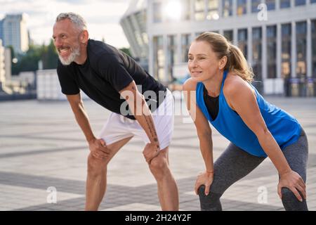 Active middle aged couple, man and woman resting, taking a short break while running together in the city on a summer day Stock Photo
