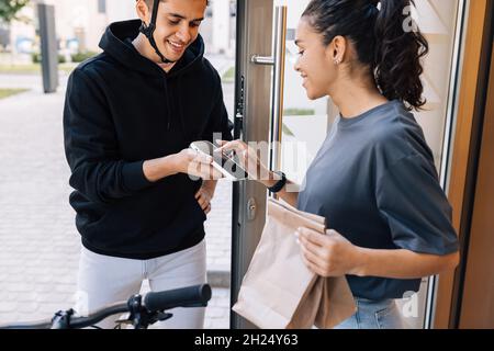 Woman receiving food delivery at the doorway. Young female signs for delivery on a smartphone. Stock Photo