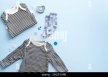 Flat lay composition with marine style baby clothes kit on pastel blue background. Striped kids bodysuit, shirst, socks. Stock Photo