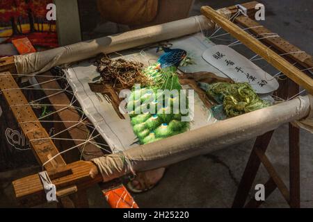 An elaborate needlework wallhanging of a peacock being hand-stitched in Guilin, China. Stock Photo
