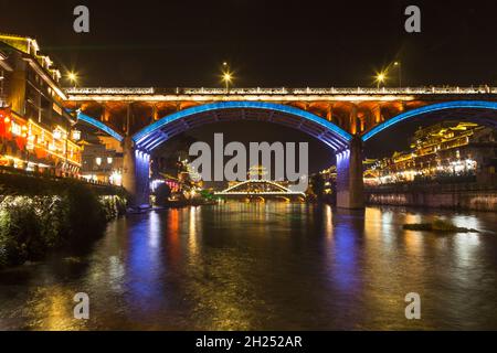 The hIghway bridge frames the Fenghuang Bridge lit up at night in Fenghuang, China. Stock Photo