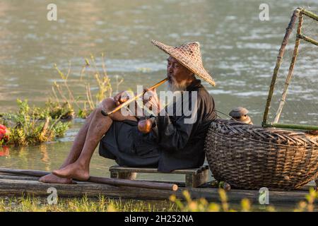 Elderly traditional cormorant fisherman smokes a wooden pipe on his raft on the Li River, Xingping, China. Stock Photo