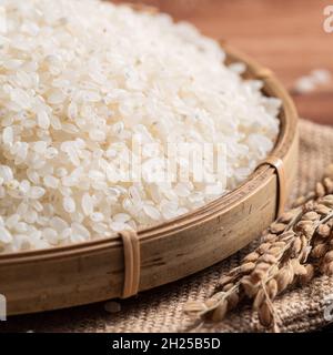 Raw white polished milled edible rice on wooden table background in a bowl, organic design concept. Stock Photo