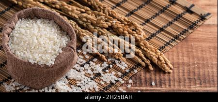 Raw white polished milled edible rice on wooden table background in a bowl, organic design concept. Stock Photo