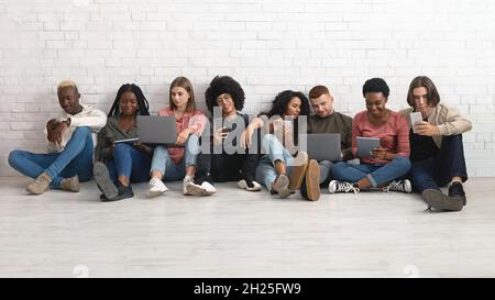 Happy multiethnic millennials using gadgets while spending time together Stock Photo