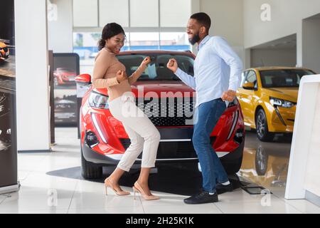 Overjoyed Black Couple Celebrating Buying New Car, Dancing In Dealership Office Stock Photo