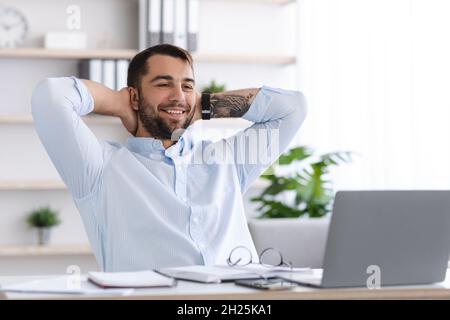 Smiling mature european male with beard take a break from work at laptop in office or living room Stock Photo