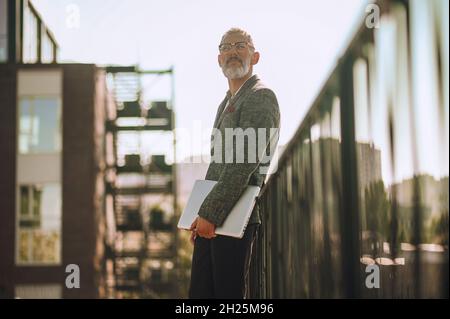 Bespectacled Caucasian man with the laptop looking into the distance Stock Photo