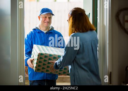 Delivery man bringing holiday packages. Woman at home standing in doorway, receiving parcels for Christmas gifts. Stock Photo