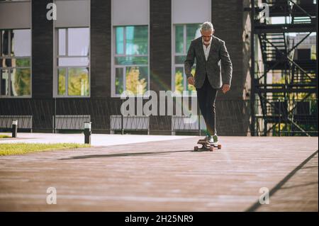 Focused bearded gray-haired male skateboarder skateboarding outside Stock Photo