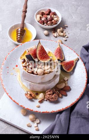 Gourmet appetizer of white brie cheese or camembert with fresh figs, nuts and honey on gray concrete background Stock Photo