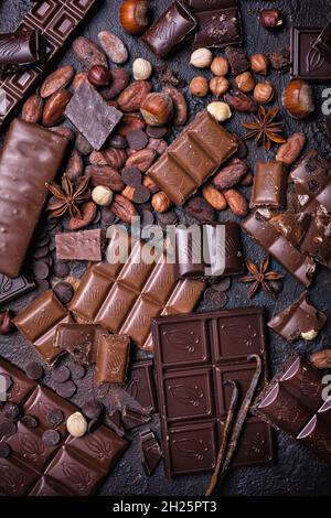 Pieces of broken tasty milk and dark chocolate bars with cocoa beans and hazelnut on black concrete background Stock Photo