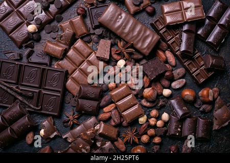 Pieces of broken tasty milk and dark chocolate bars with cocoa beans and hazelnut on black concrete background Stock Photo
