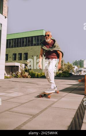 Gray-haired bearded man skateboarding in the street Stock Photo