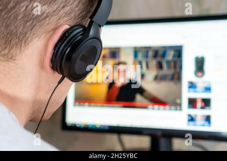 Close-up of a man with headphones watching a video on the Internet on a computer, photo from the back Stock Photo