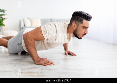 Millennial Arab man doing push ups, standing in plank pose, doing strength exercises at home. Domestic workout concept Stock Photo