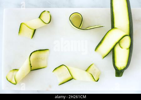 Zucchini, Courgette ribbons and zucchini, courgette on white marble board with copy space. Top view. Stock Photo