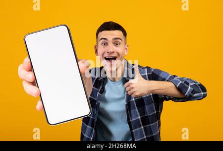 Positive millennial man showing smartphone and thumb up, mockup Stock Photo
