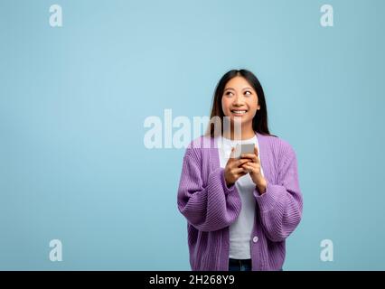 Mobile application concept. Young asian lady using modern smartphone and looking at copy space, blue background Stock Photo
