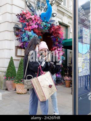 London, Greater London, England, October 05 2021: Fashionable young women with shopping bags check their phones in Covent Garden. One wears sunglasses Stock Photo