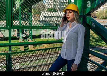Beautiful young woman engineer or supervisor, wearing a safety helmet, talking on a cell phone while taking a short break inspecting a railroad pedest Stock Photo