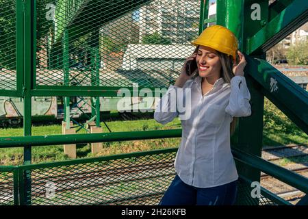 Beautiful young woman engineer or supervisor, wearing a safety helmet, talking on a cell phone while taking a short break inspecting a railroad pedest Stock Photo