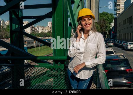 Beautiful young woman engineer or supervisor, wearing a safety helmet, talking on a cell phone while taking a short break inspecting a railroad pedest Stock Photo