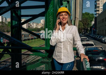Beautiful young woman engineer or supervisor, wearing a safety helmet, talking on a cell phone while taking a short break inspecting a railroad pedest Stock Photo